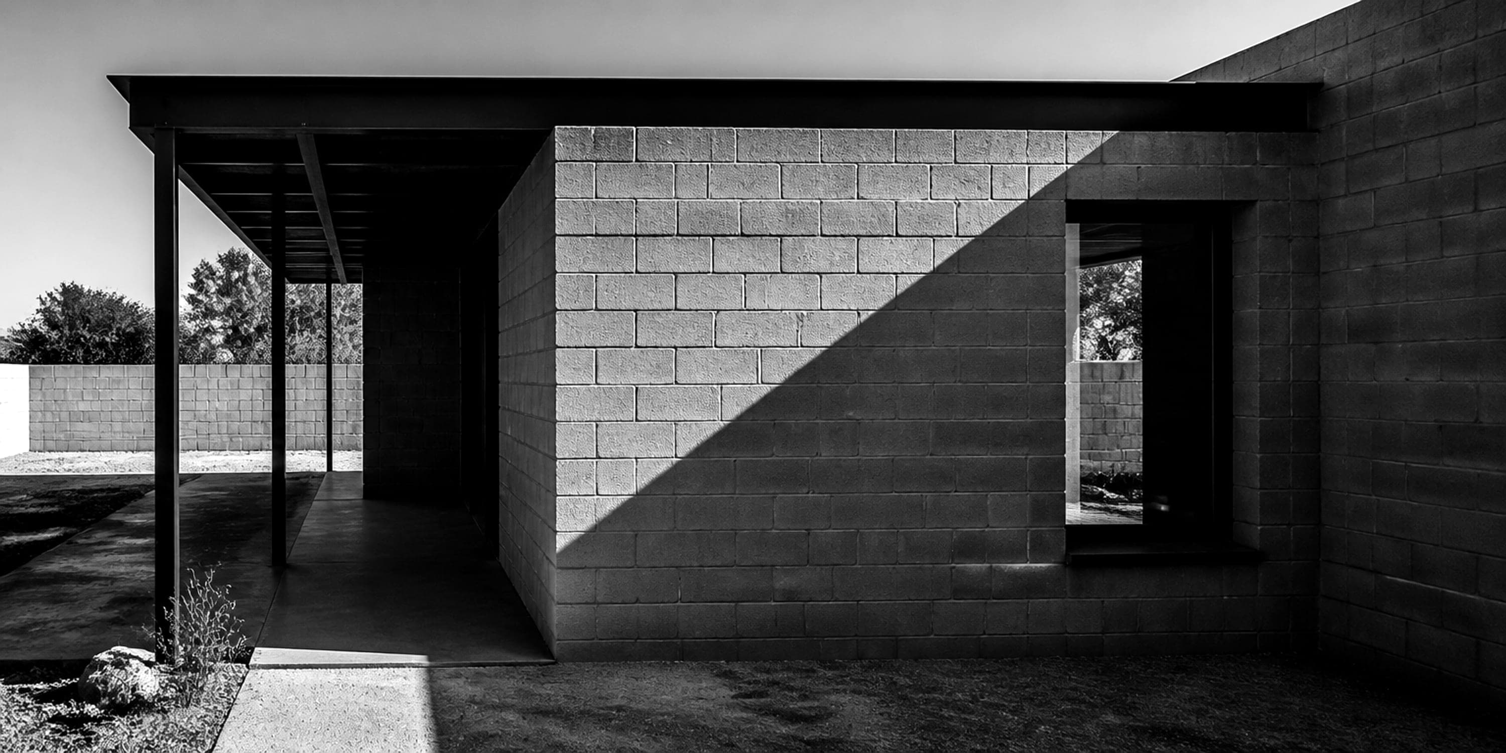 A house built in grey concrete masonry block, the wall face lit by hard afternoon sun