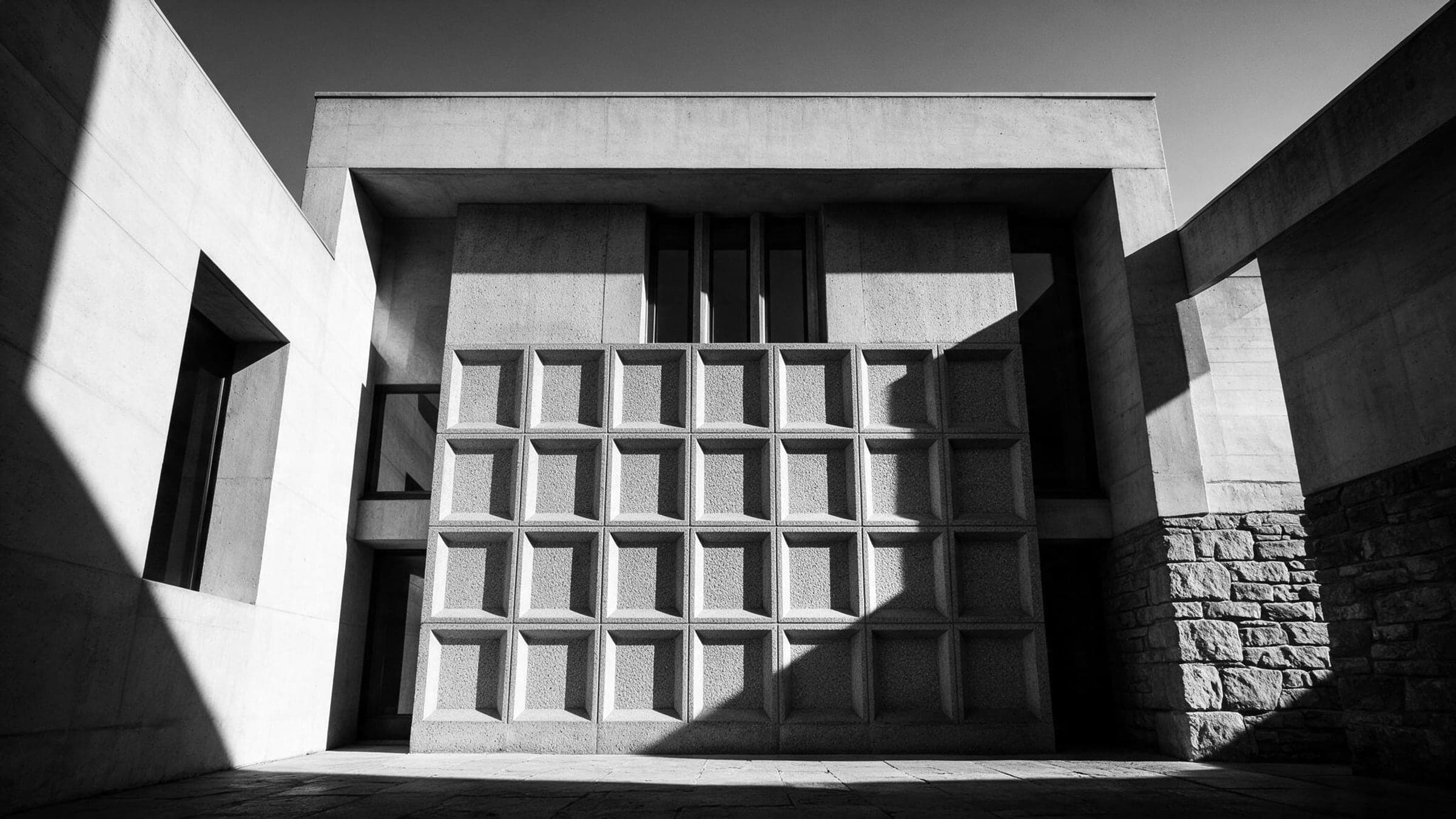 Cast concrete architecture in hard raking sun, deep shadow across a coffered panel